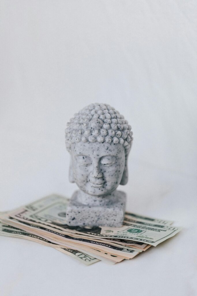A stone Buddha bust placed on a stack of various US dollar bills, symbolizing harmony and finance.